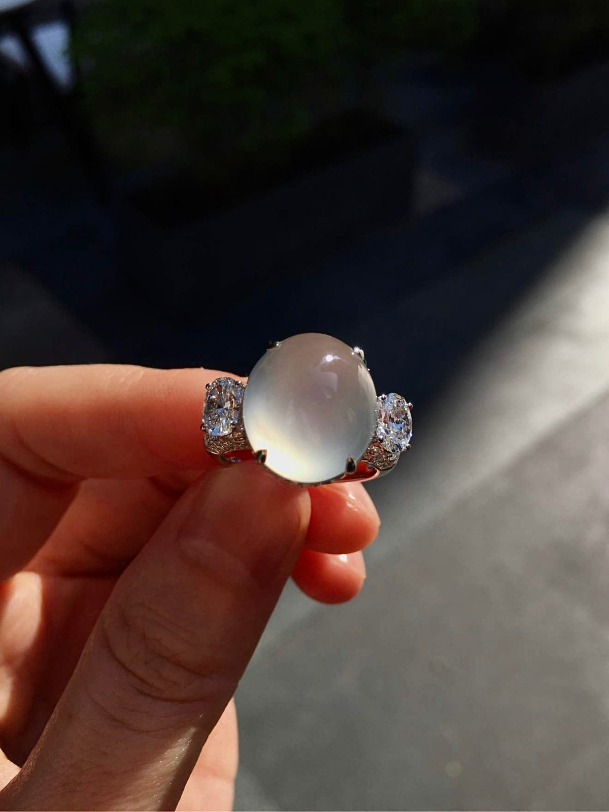 Oval jadeite cabochon ring held in daylight, showing its translucency and diamond accents