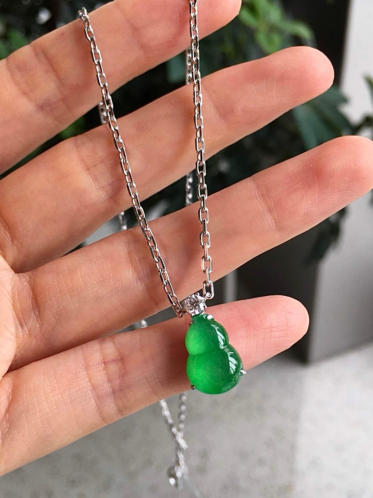 Side view of green jadeite gourd carving beside the included linked chain
