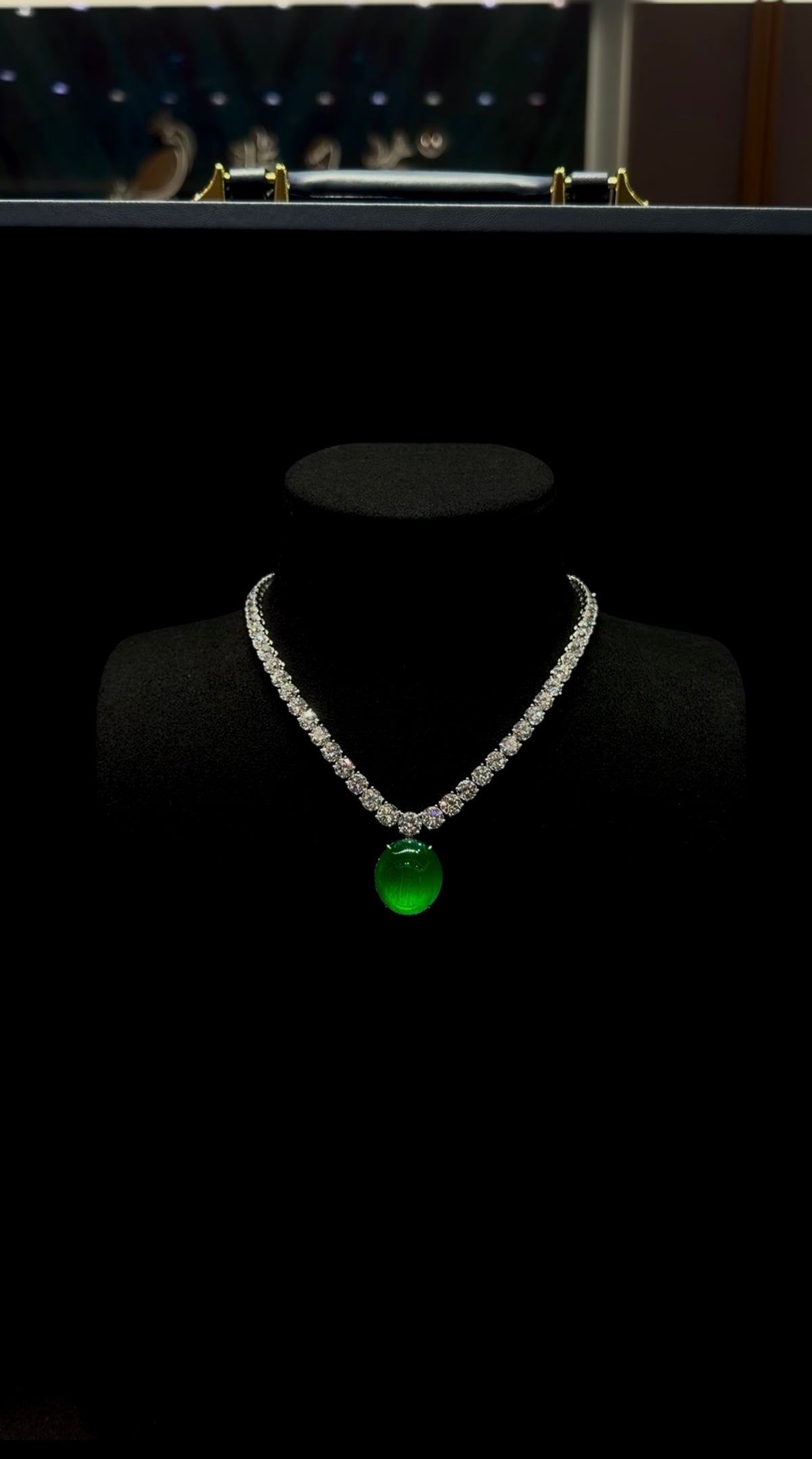 Oval imperial green jadeite cabochon suspended from a diamond-set necklace, shown on a black display bust at Feiyuehui Jewelry.